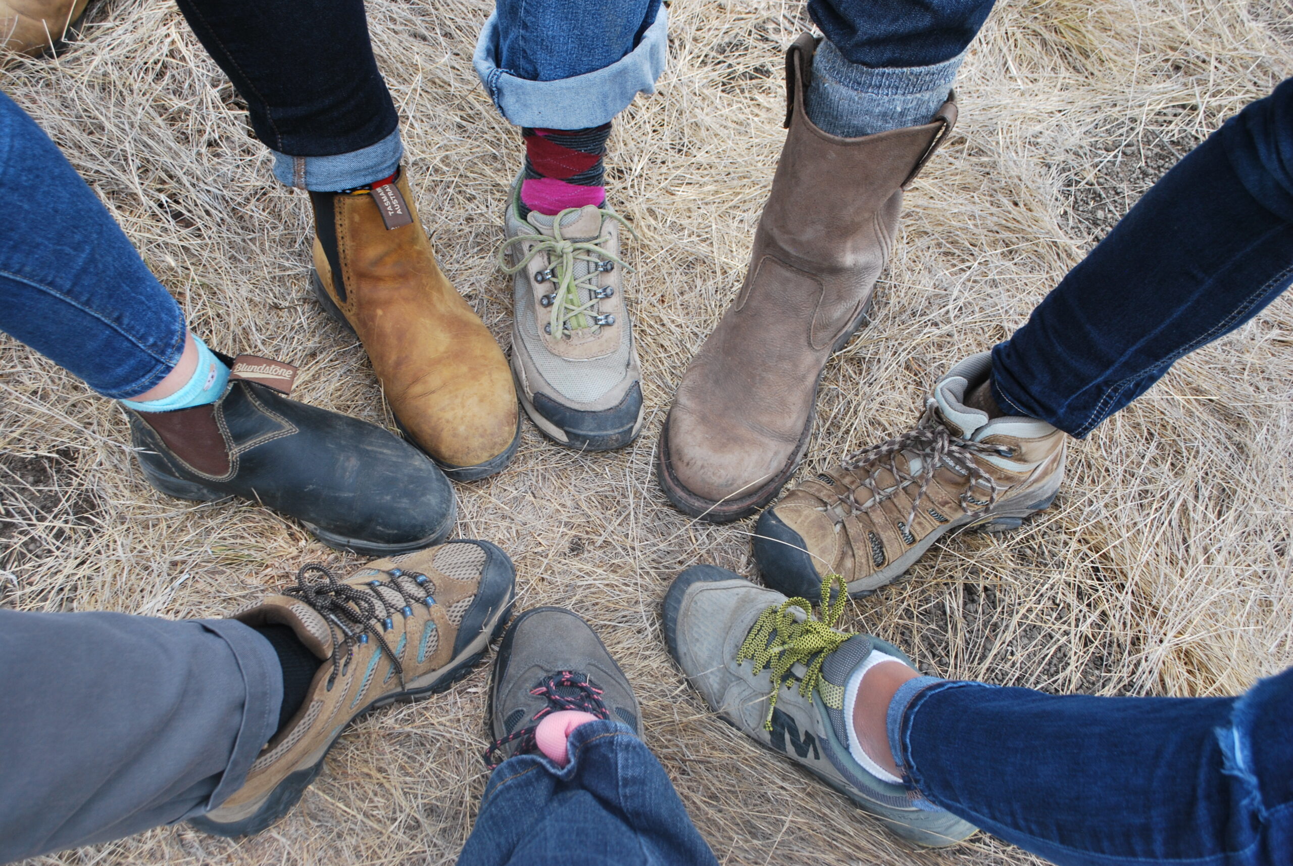 Boots on the ground together Tight circle of eight different feet on the ground, each in different footwear.