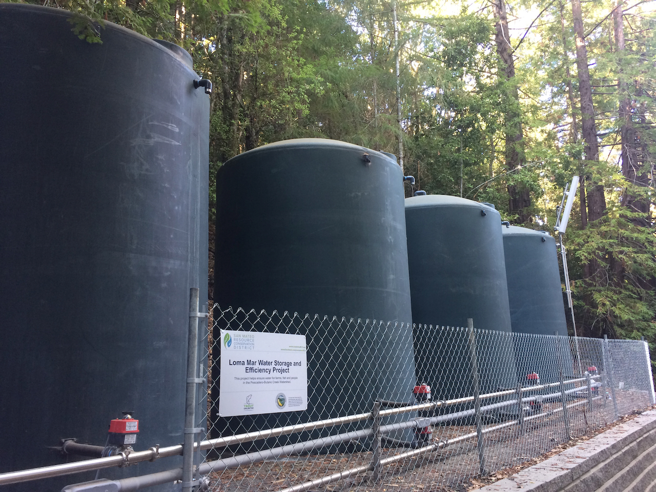 Water storage Large black tanks behind a chain link fence with a sign labelling them as the Loma Mar Water Storage and Efficiency Project..